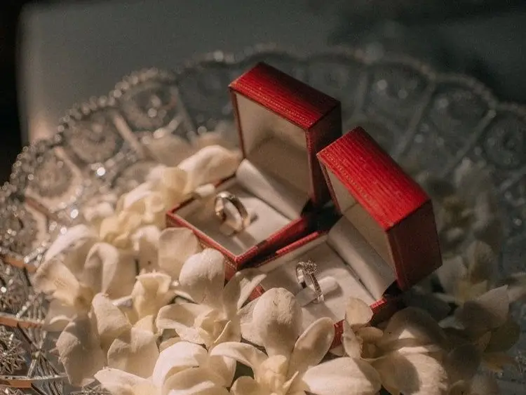 Two red ring boxes with rings on a cut-glass bowl filled with white orchid petals