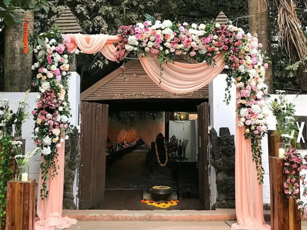 Gate arch of pink and white flowers with peach drapes over a wooden doorway