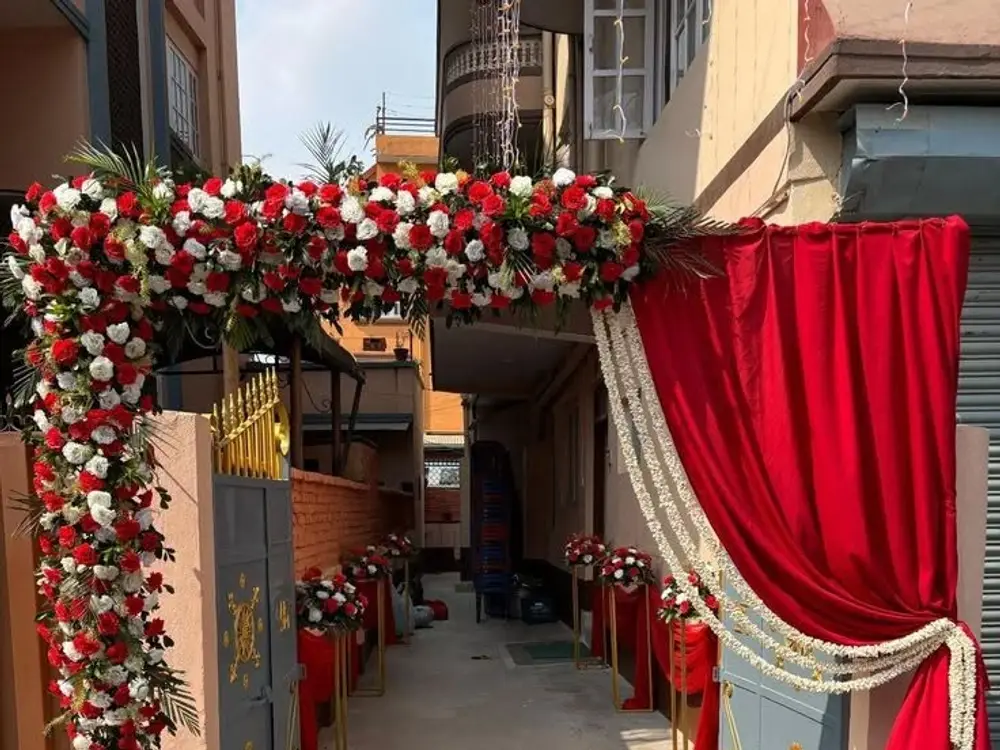 Gate arch of red and white roses with red drapes at the mouth of a residential lane