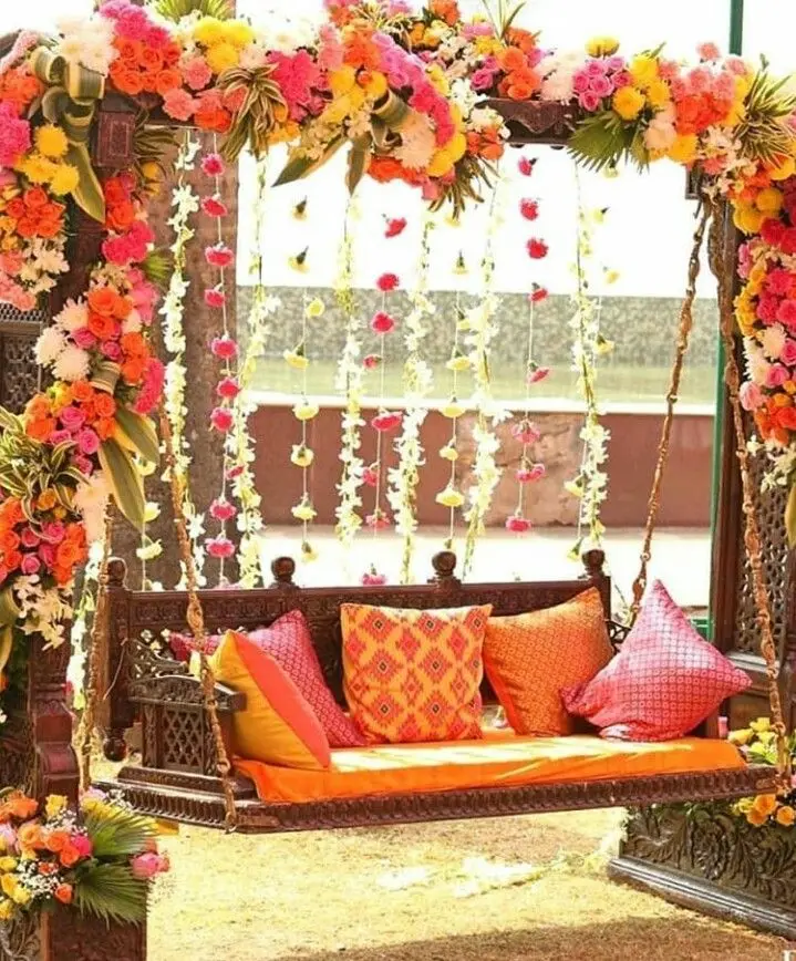 Carved wooden swing with orange and pink cushions, flower arch and hanging flower strings