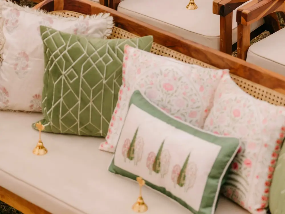 Cane sofa with ivory cushion and green and pink block-print pillows in a row of wooden chairs