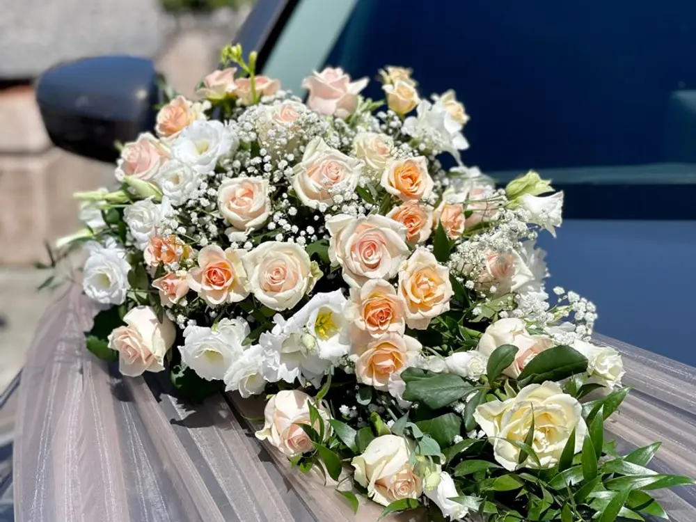 Cream and peach roses with baby's breath on a dark car bonnet over grey tulle