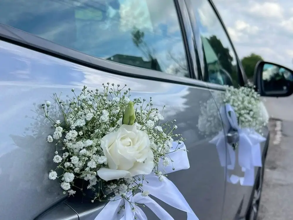 White rose with baby's breath and a white ribbon tied to a car door handle