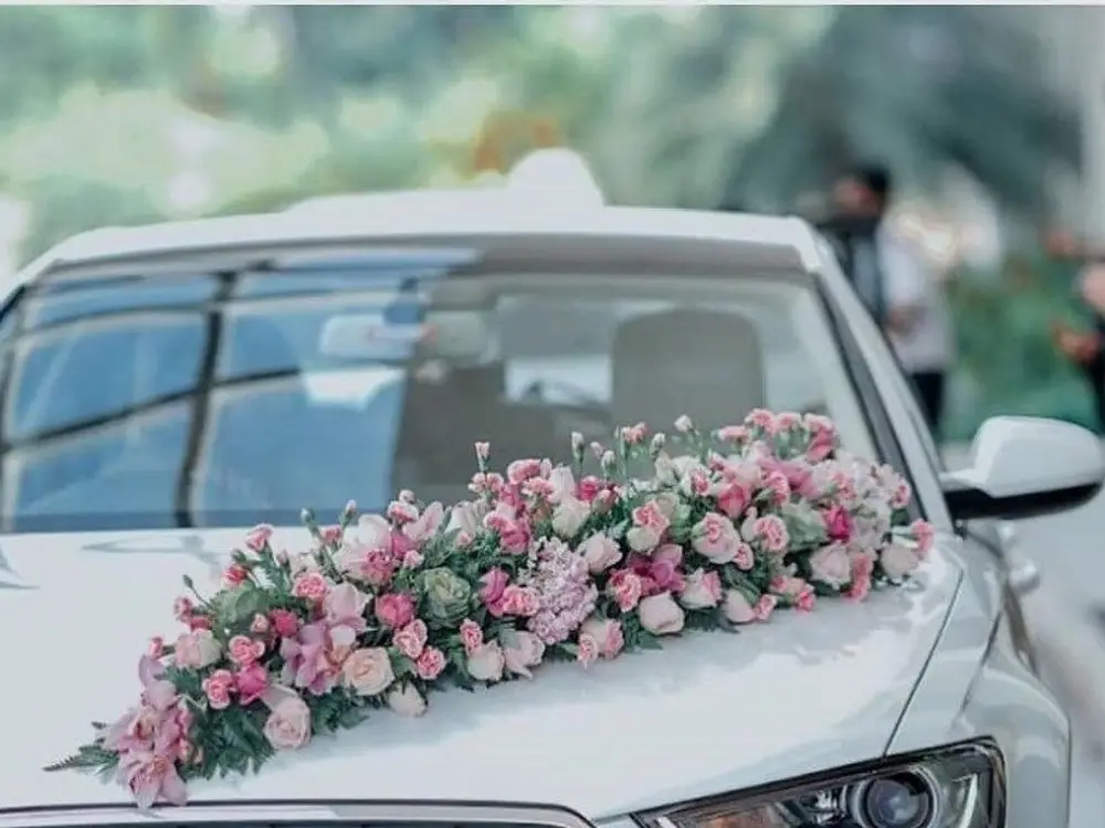 Pink roses and white flowers in a long spray along the bonnet of a white car