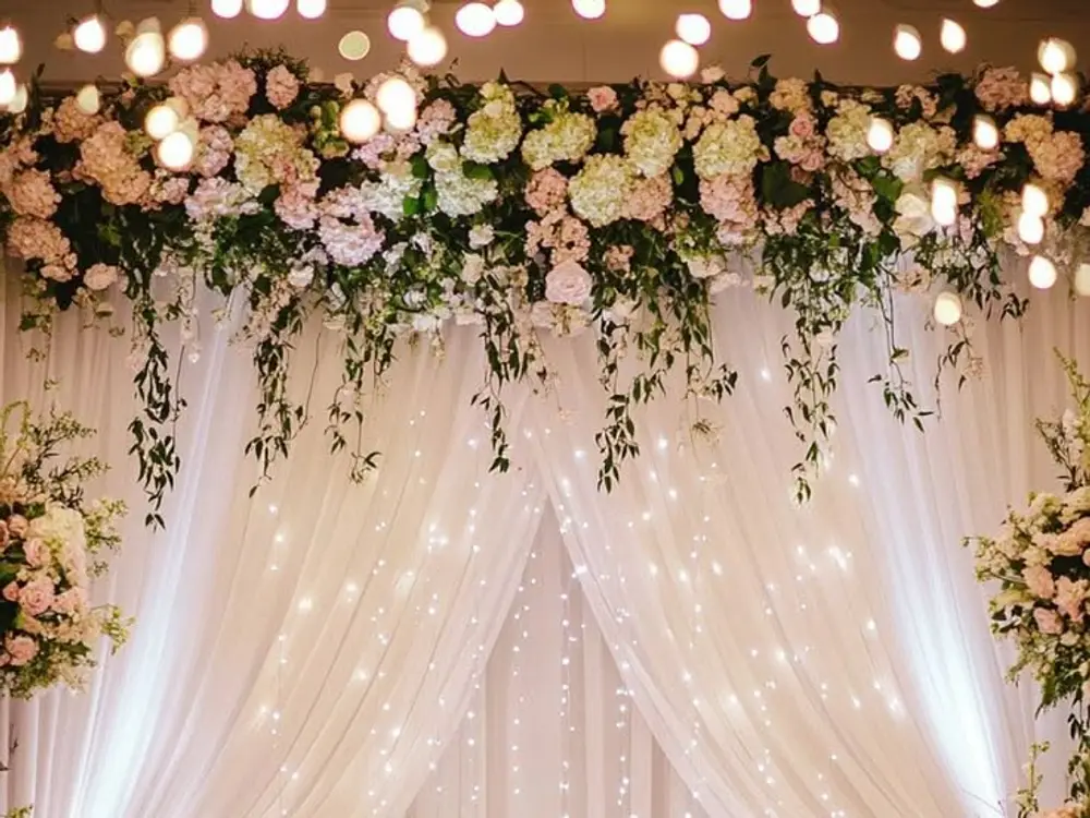 White drapes with fairy lights and a hanging green and pink flower border