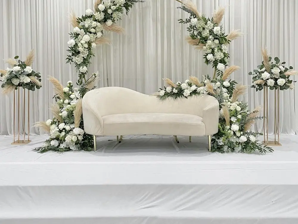 Cream sofa in front of a white drape with a gold ring frame wrapped in white flowers and pampas grass