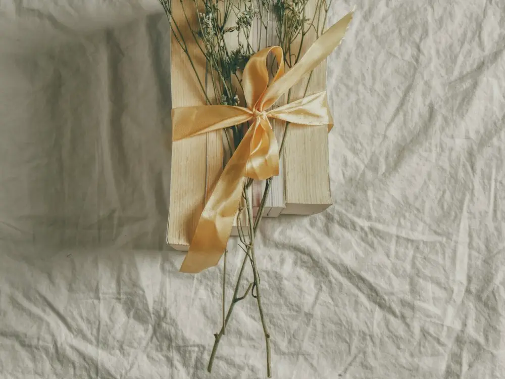 Small gift tied with a gold satin ribbon and dried flowers on creased cream linen