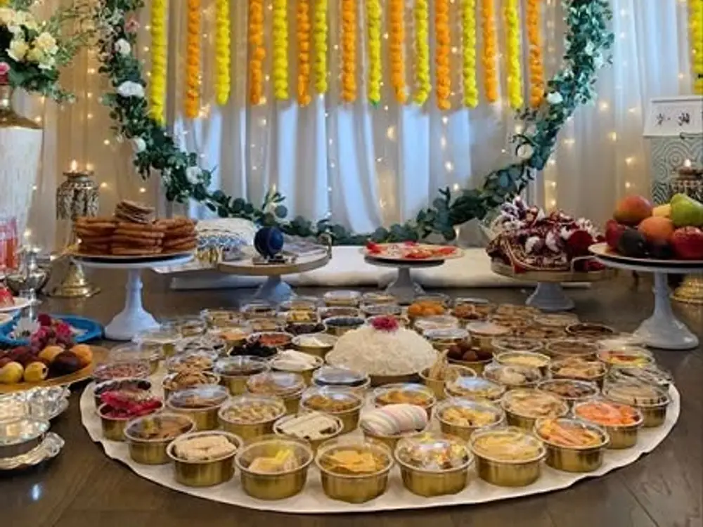 Annaprashan stage with a green ring, yellow marigold curtain strings, fairy lights and a thali spread of first foods