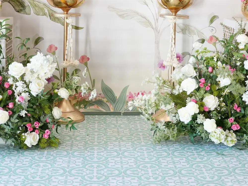 White and pink flowers with green leaves beside gold lotus lamps on a patterned floor