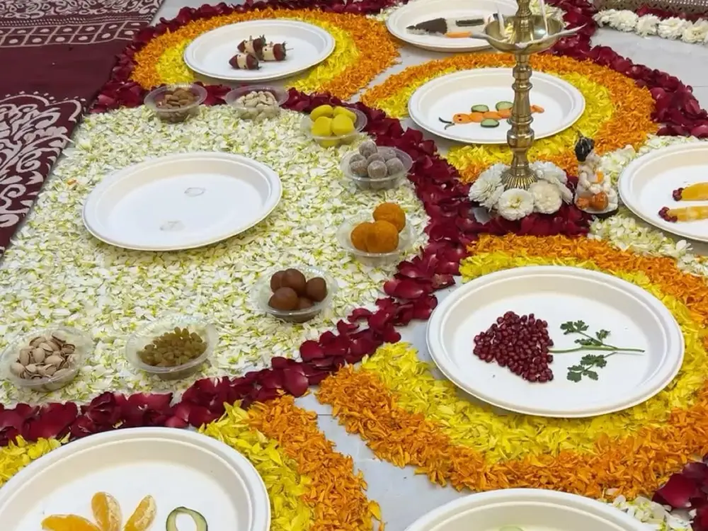 Plates of fruit and sweets laid on a rangoli of yellow, orange and red petals