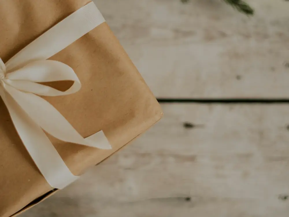Kraft wrapped gift with a cream ribbon on a whitewashed wooden table