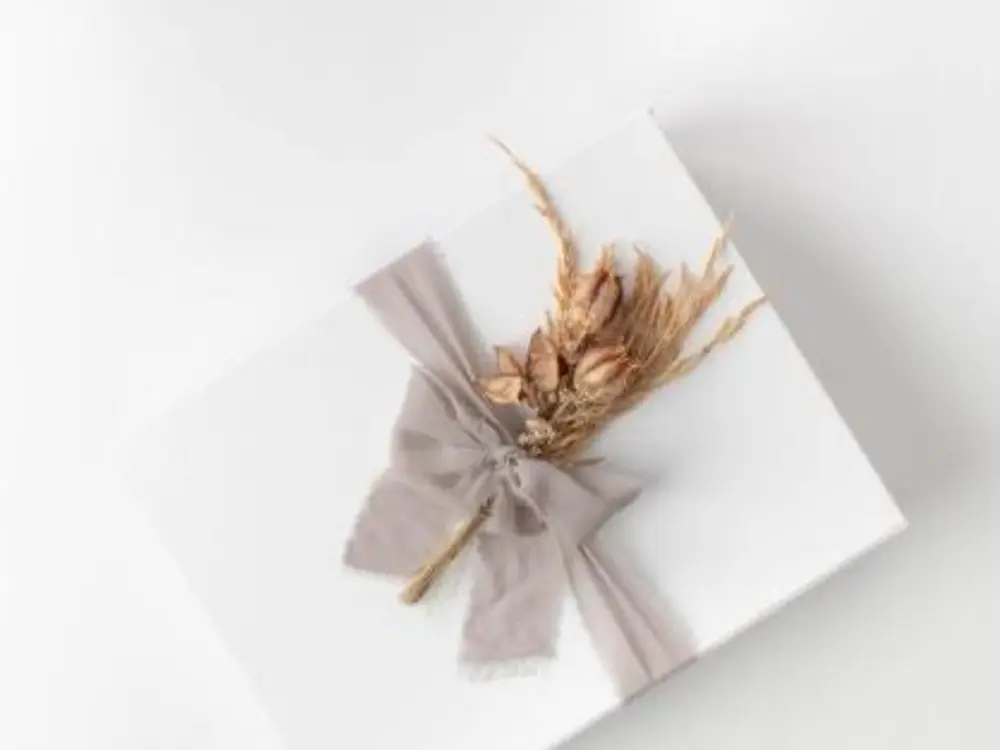White gift box tied with a grey silk ribbon and a small bunch of dried grasses