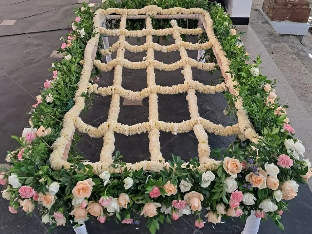 Flower canopy frame with a rope net, green leaves and peach, pink and white roses on a dark floor