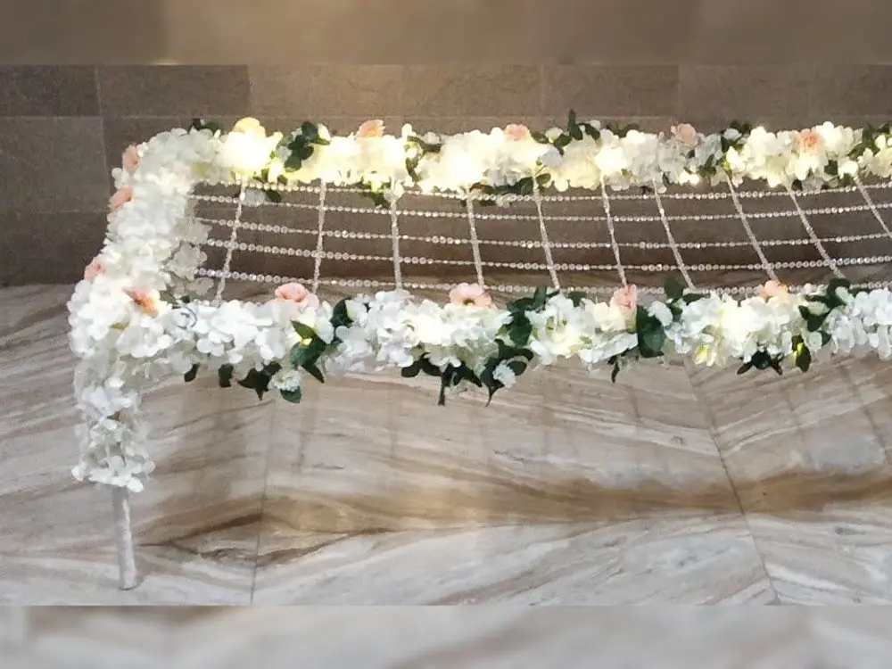 Canopy frame edged with white roses and green leaves and lit with small lights over a beaded net