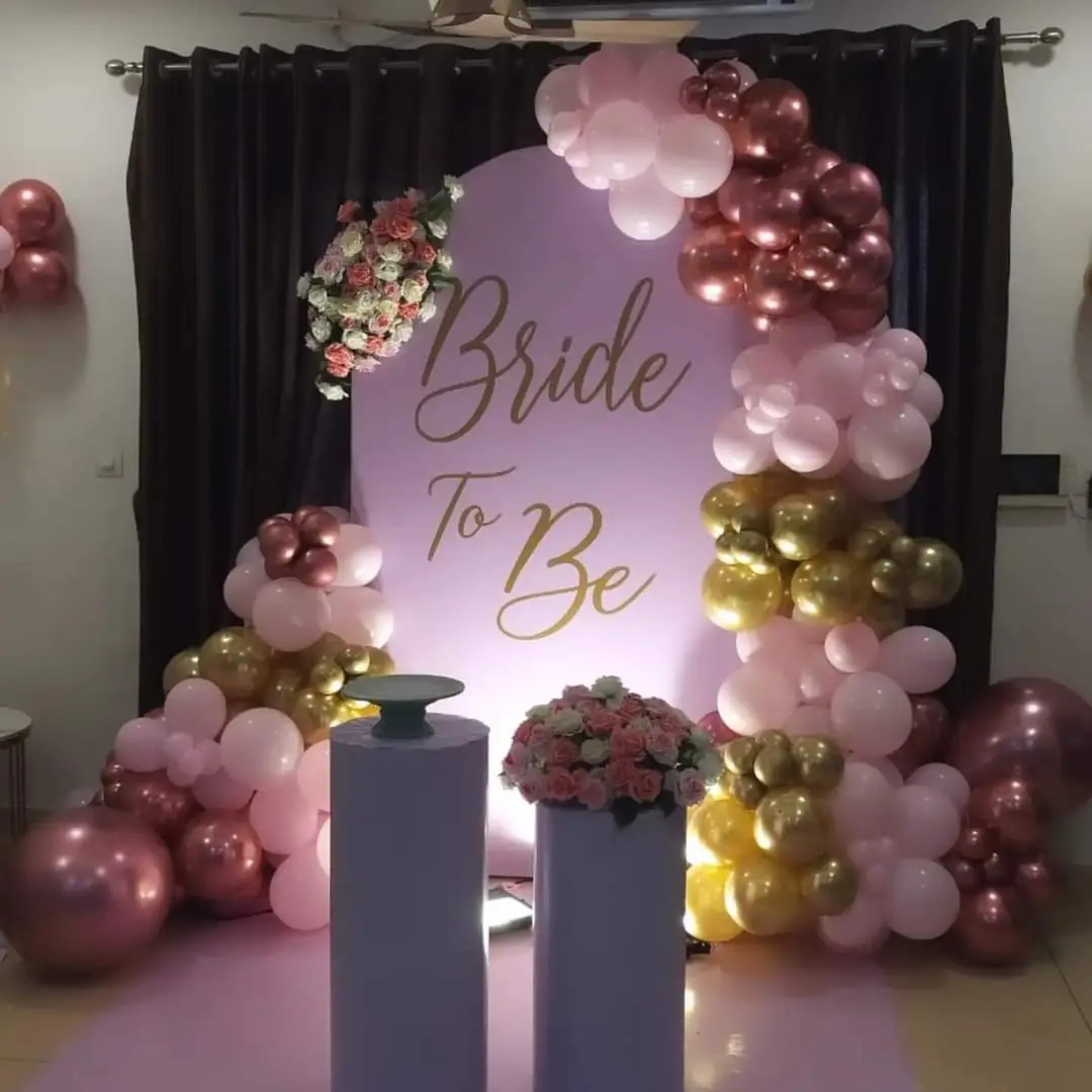Pink and gold balloon arch around a Bride to Be backdrop with two white pillars and pink roses