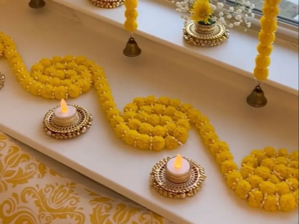 Window ledge with a yellow marigold garland, two tea lights and small vases of yellow flowers