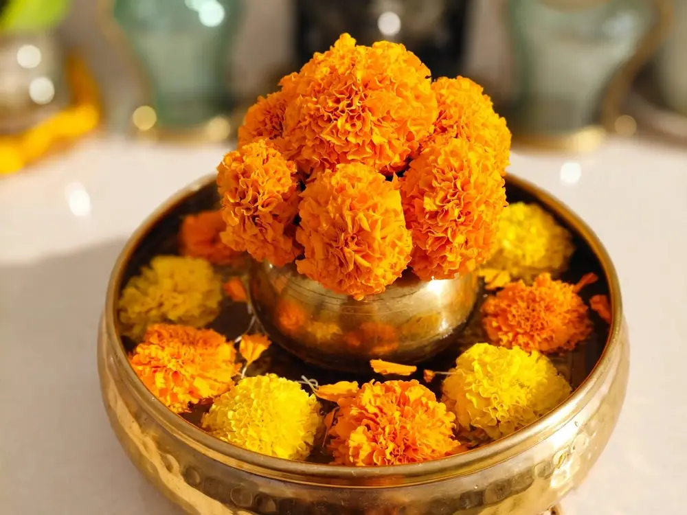 Brass urli with marigold blooms and a small brass pot of flowers on a white marble counter