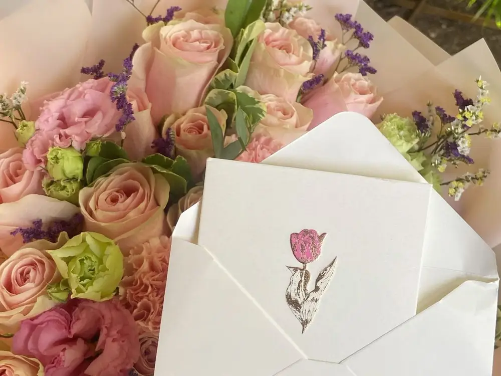 Pink roses and lisianthus in cream wrapping with a small cream card in an envelope