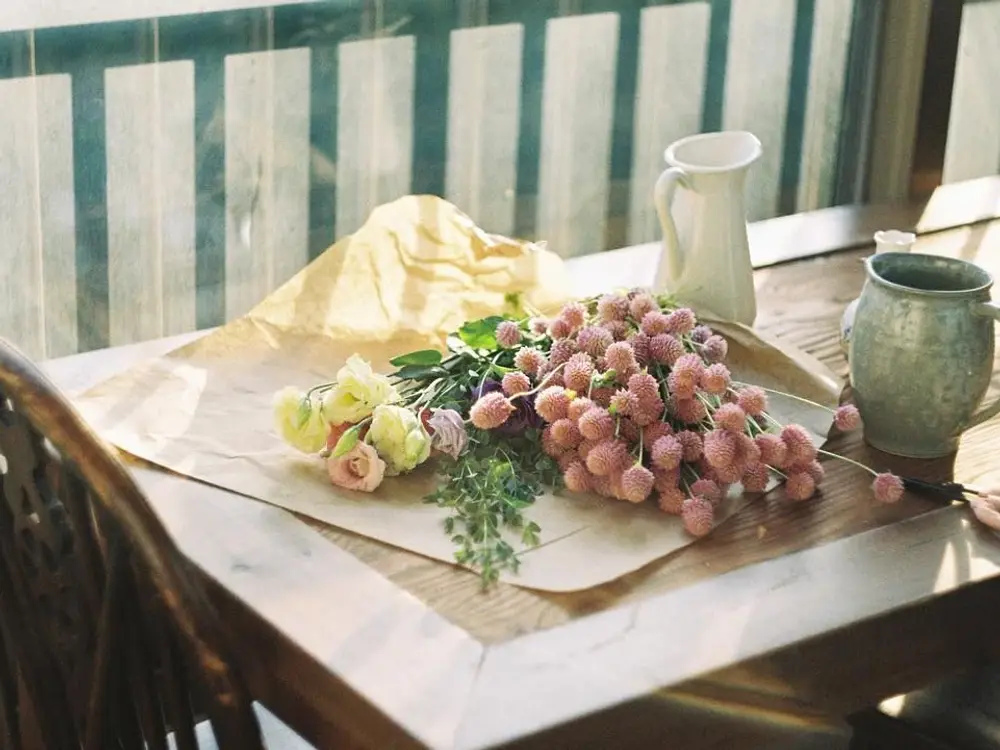 Pink pom-pom flowers and cream lisianthus lying on kraft paper on a wooden table by a window