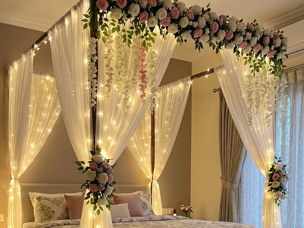 Four-poster bed with white drapes, fairy lights and a flower garland across the top