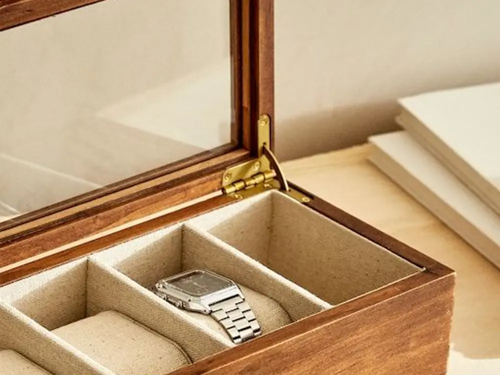 Open walnut watch box with a steel watch on a linen-lined cushion