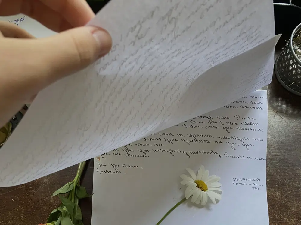 A handwritten letter on a wooden table with a single daisy laid on it
