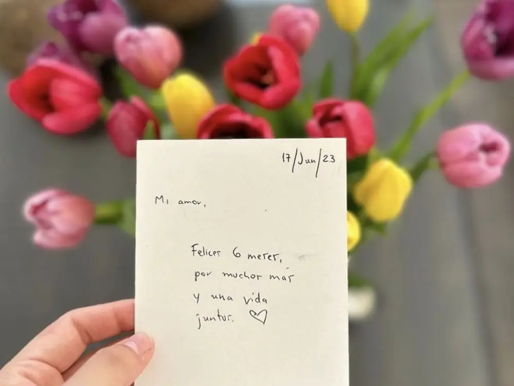 Hand holding a handwritten note in front of red, pink and yellow tulips