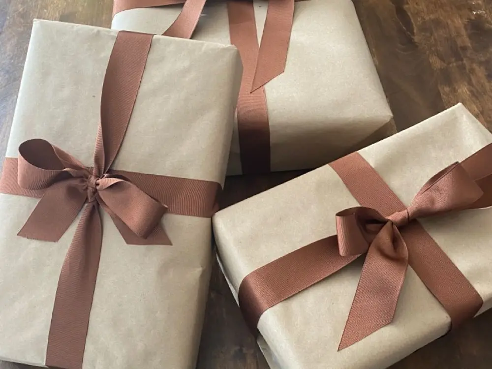 Three kraft-wrapped gift boxes tied with dusty pink ribbon on a wooden table