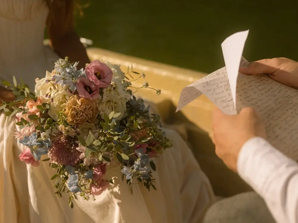 A woman reading a handwritten letter beside a pink and blue flower bouquet