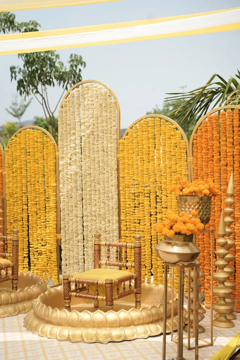 Arched panels covered in yellow, cream and orange marigold strings with gold frames on a lawn