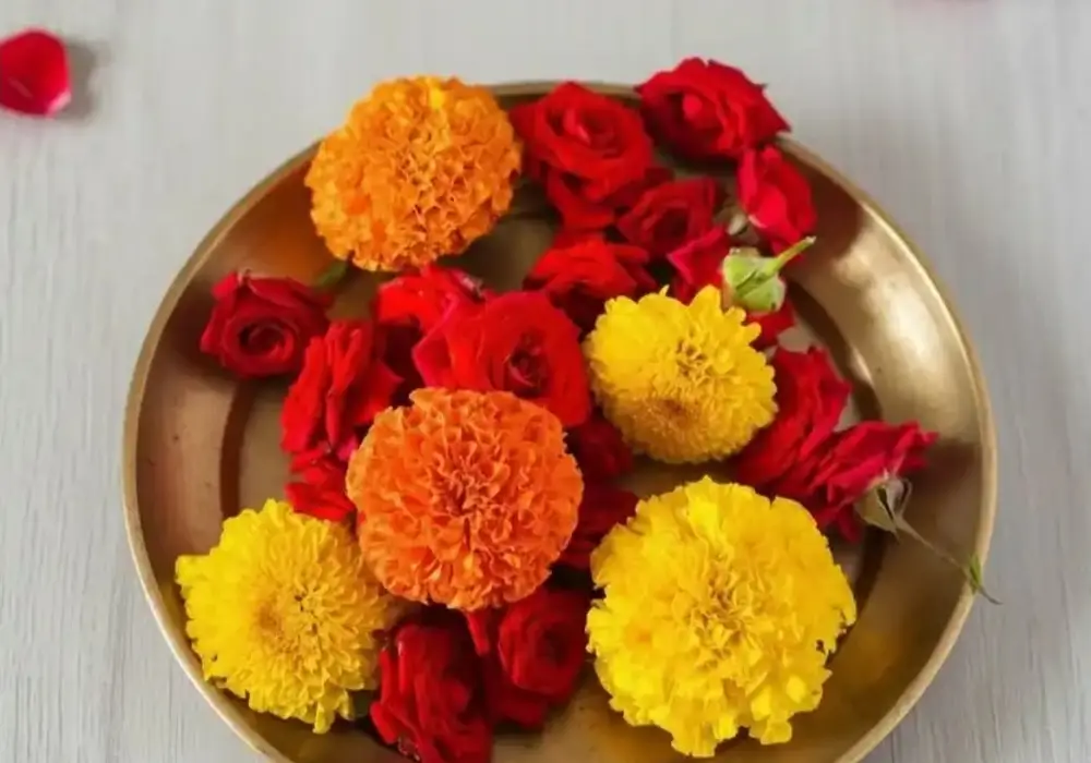 Orange and yellow marigold with red roses on a brass plate on a pale wooden table