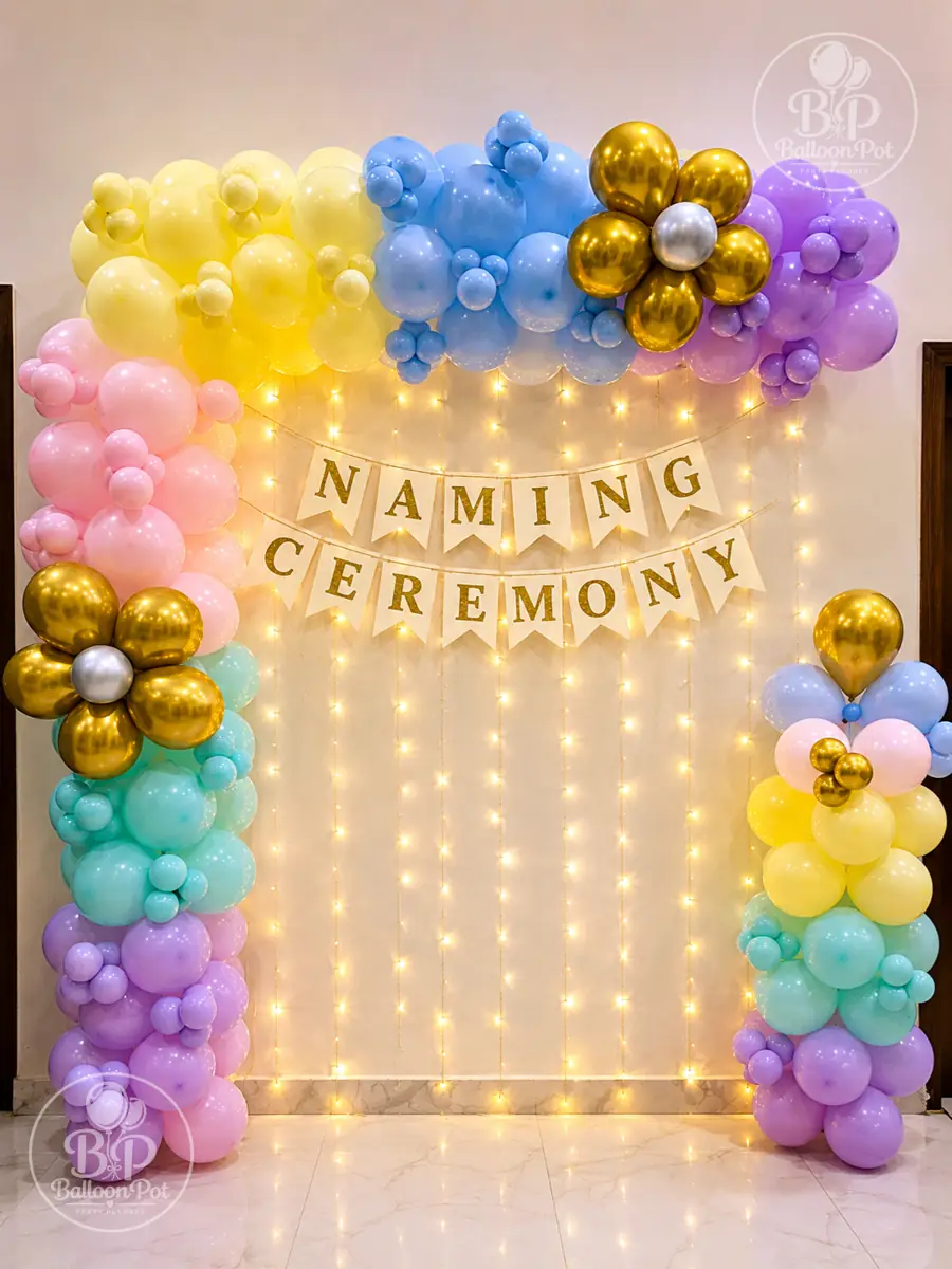 Pastel balloon arch around a Naming Ceremony bunting on a fairy light curtain