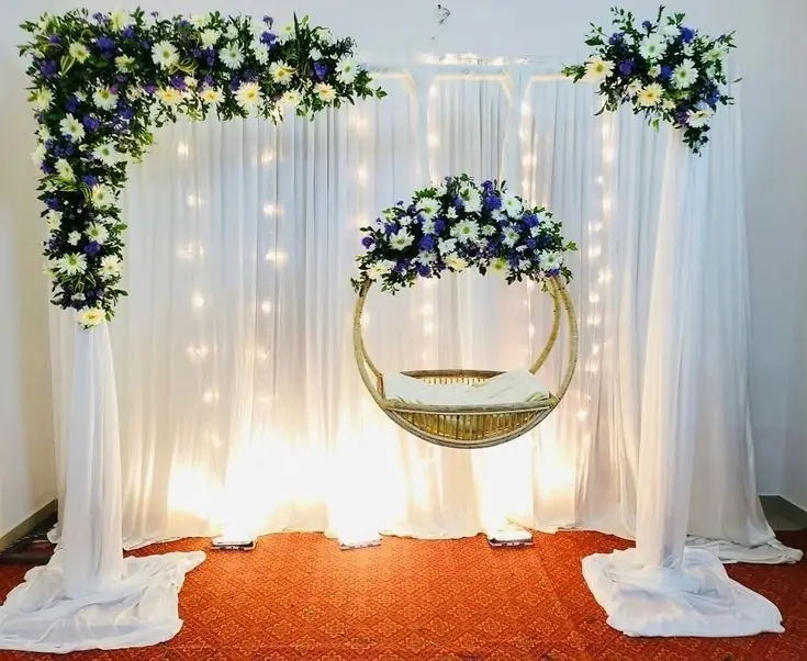 White draped frame with blue and white flower clusters and a round swing seat lit by fairy lights