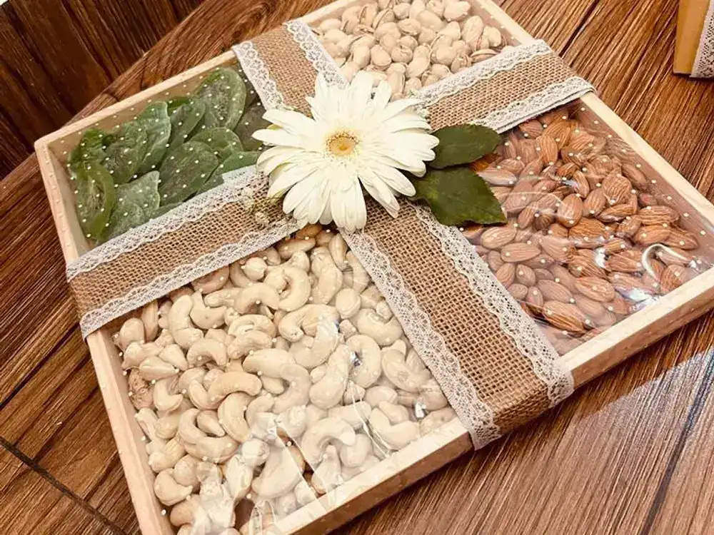 Wooden tray of cashews, almonds, pistachios and green dried fruit tied with jute ribbon and a white gerbera