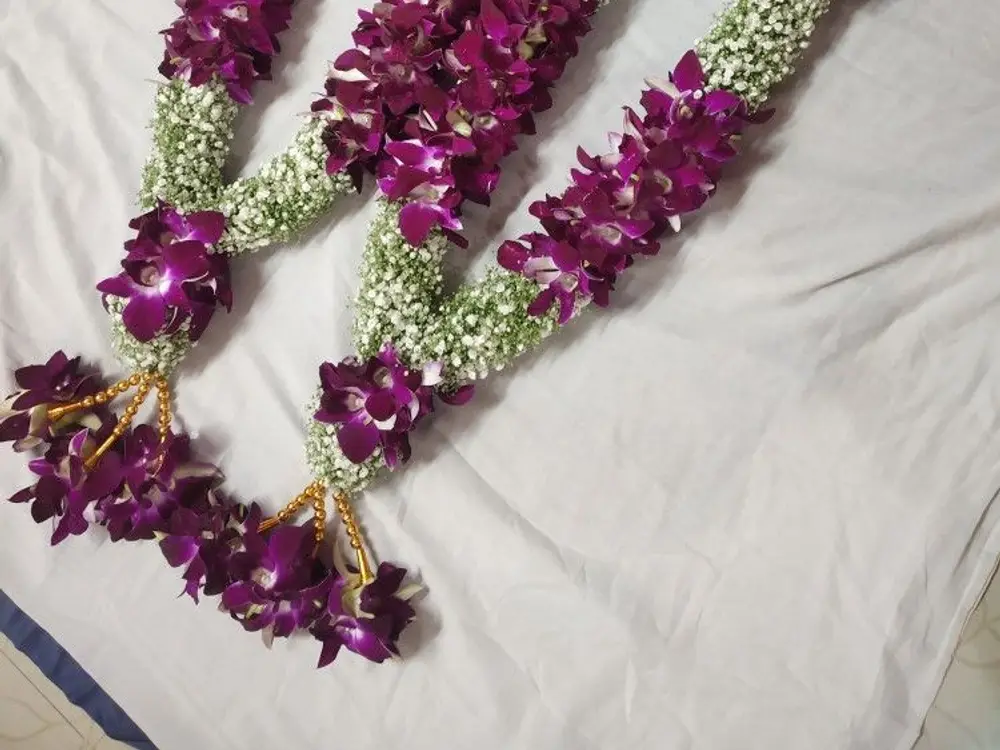 Pair of purple orchid varmalas with baby's breath and gold tassels on a cream cloth