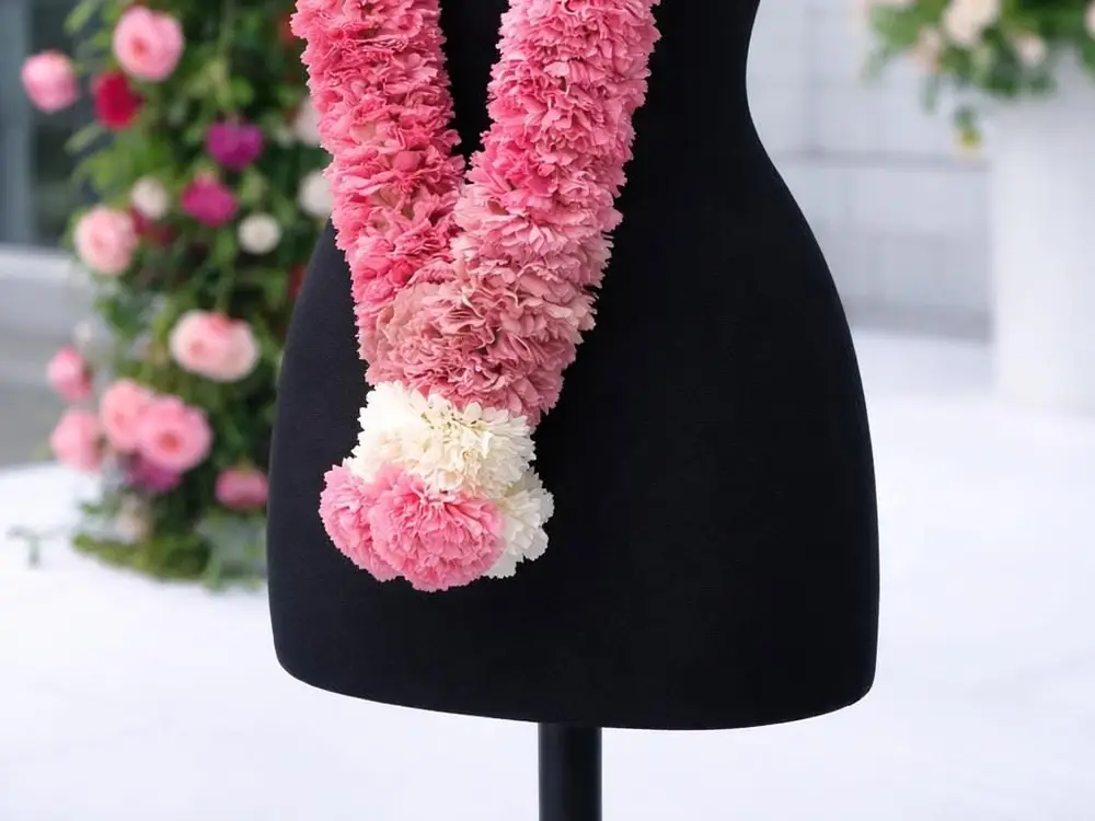 Pink and white carnation varmala hanging on a black bust with a pink pearl tassel