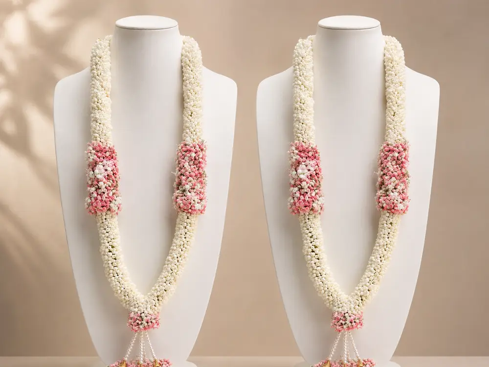 Pair of white strand varmalas with pink flower panels on white display busts
