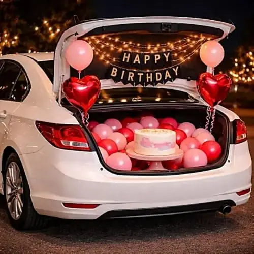 A white car boot with red and pink balloons, a cake and a Happy Birthday banner