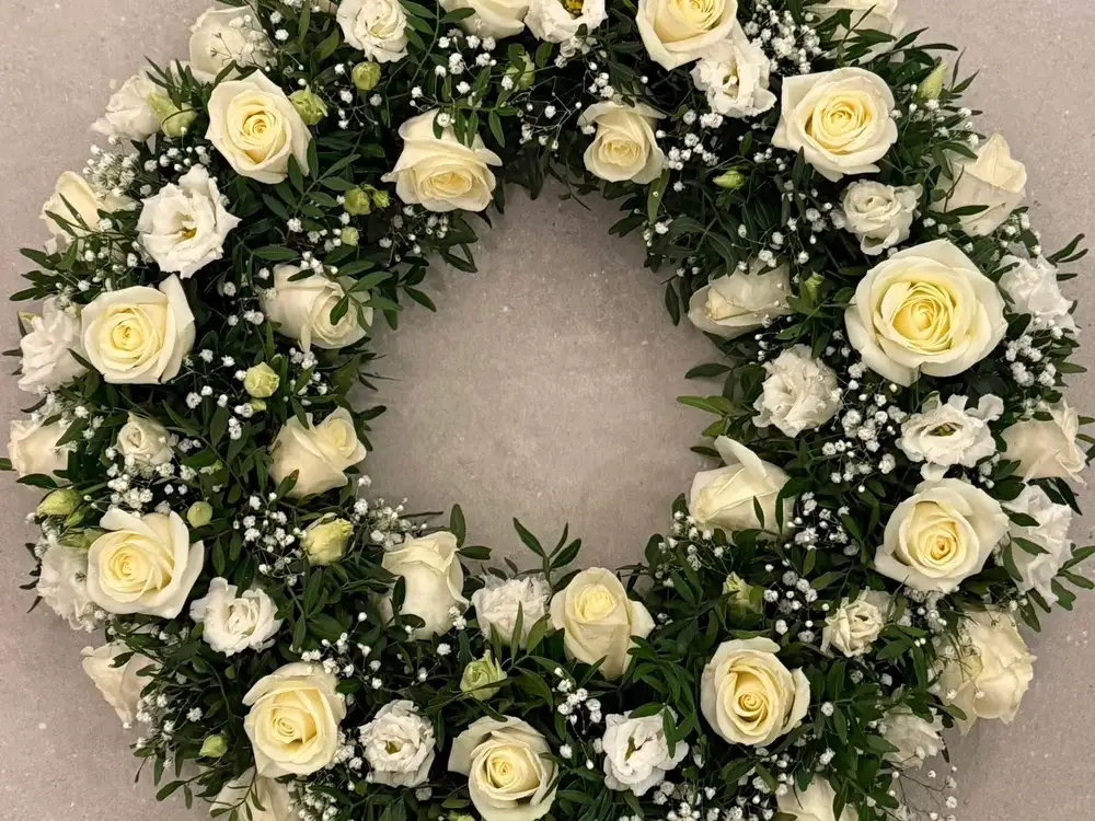 A round wreath of white roses and baby’s breath with green leaves
