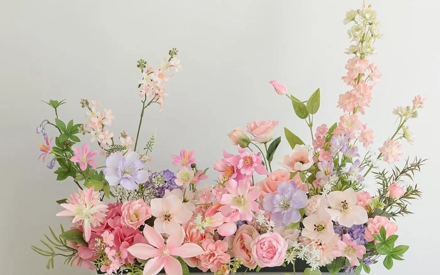 Pastel pink, peach and lilac flower arrangement on a white plinth against a pale wall