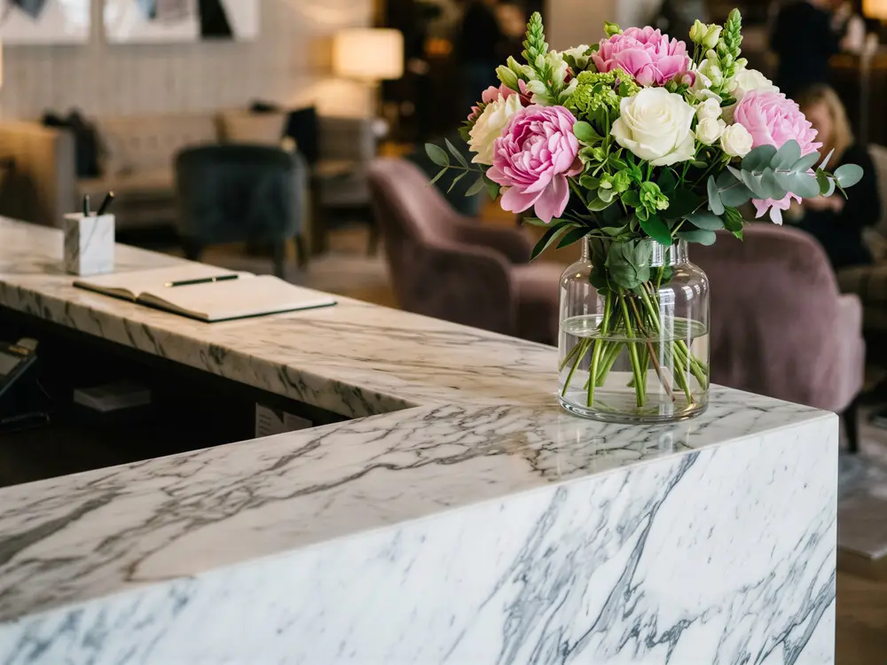 Pink peony and white rose bouquet in a glass vase on a marble hotel reception desk
