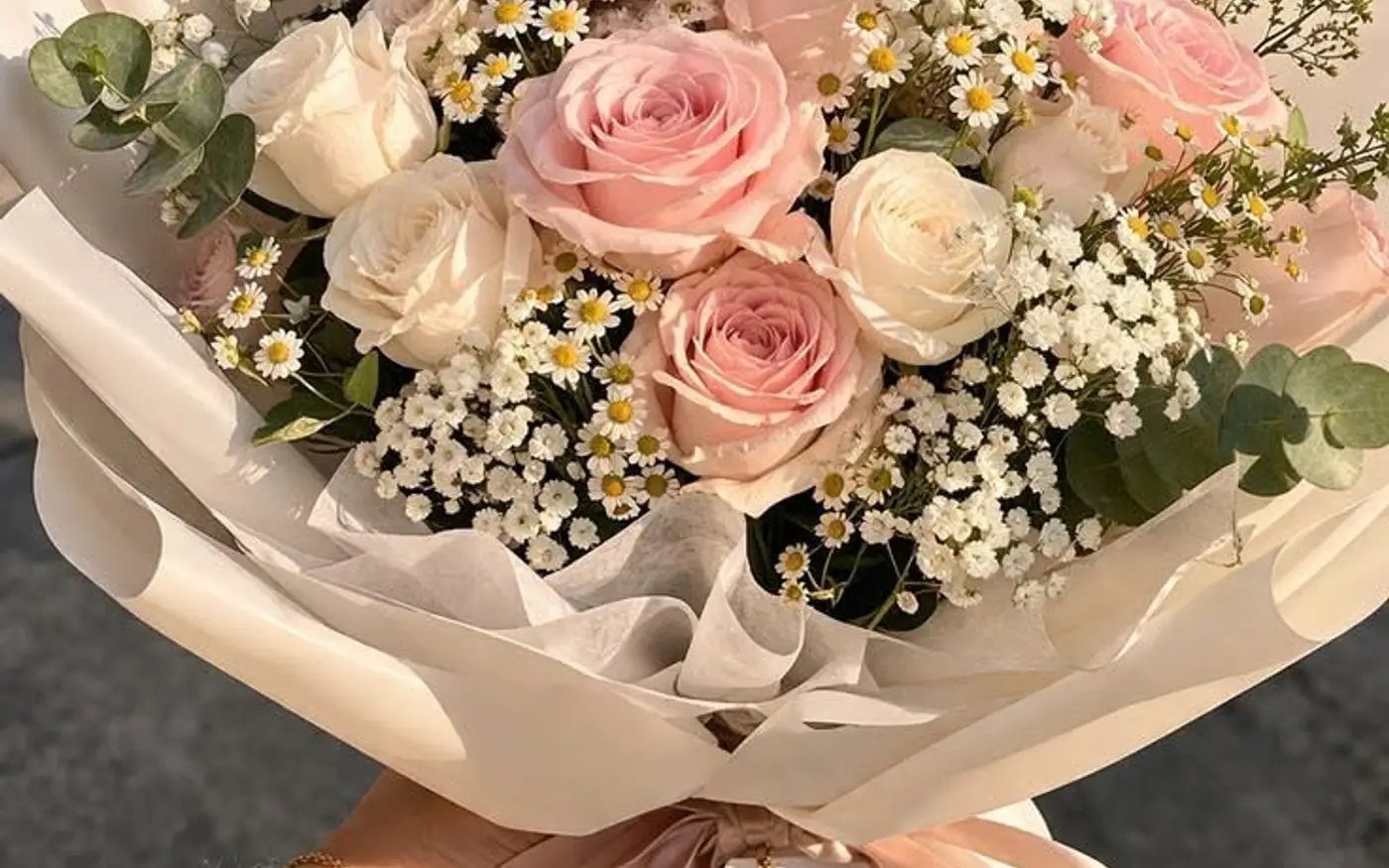 A pink wrapped bouquet of lilies, roses and baby’s breath tied with a satin ribbon