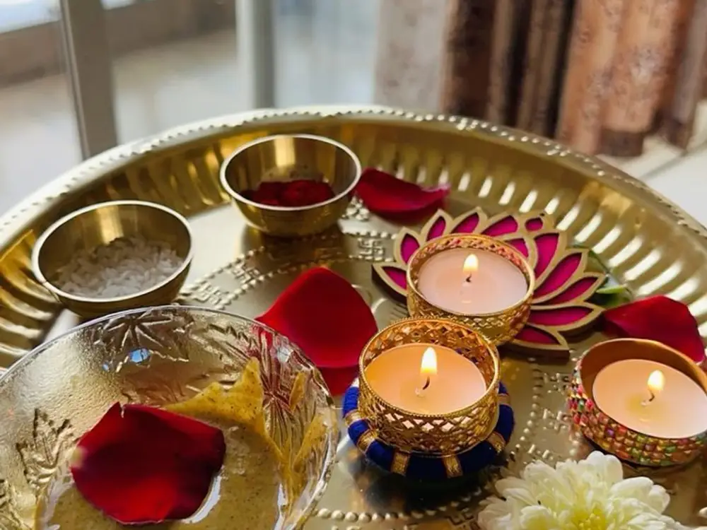 Brass puja thali with lotus diyas, red petals, rice and kumkum