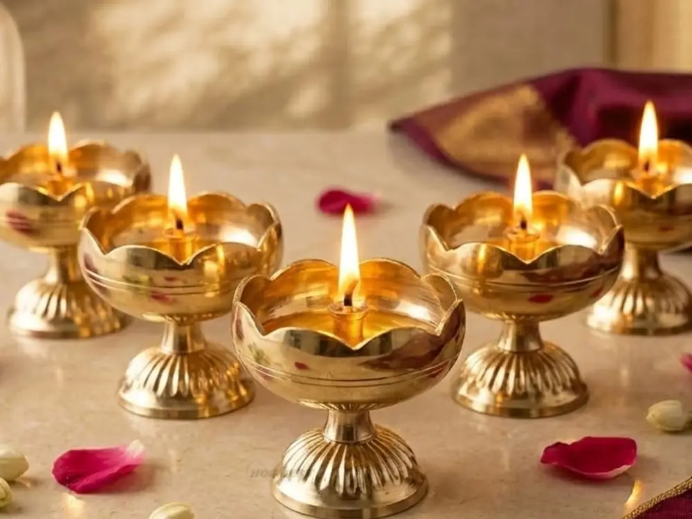 Brass lotus diyas lit on a cream surface with scattered petals