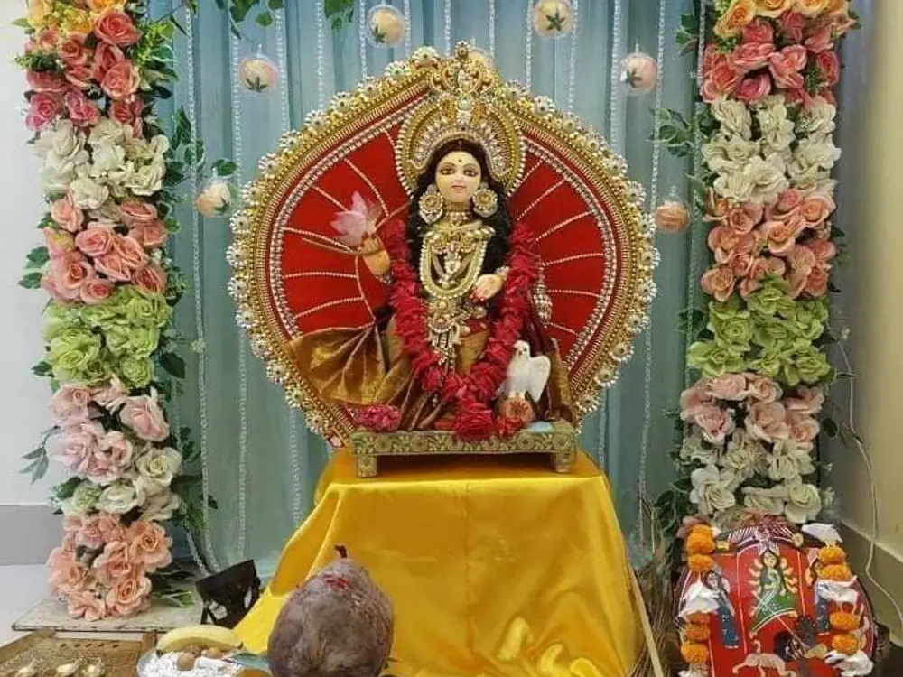 Durga idol on a yellow cloth framed by pastel roses and green hydrangeas