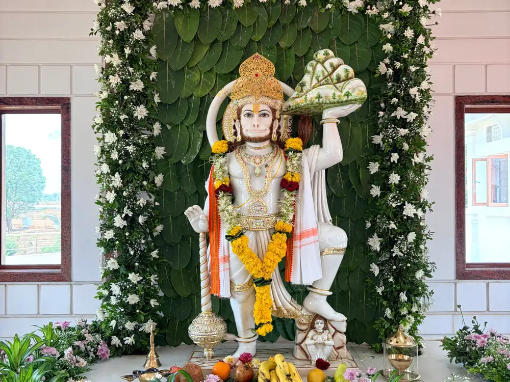 Hanuman idol in a green leaf and white flower arch with a marigold garland