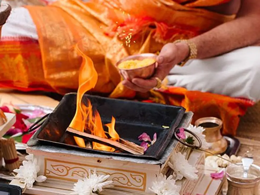 Pandit ji offering rice into a havan kund decorated with white chrysanthemums and petals