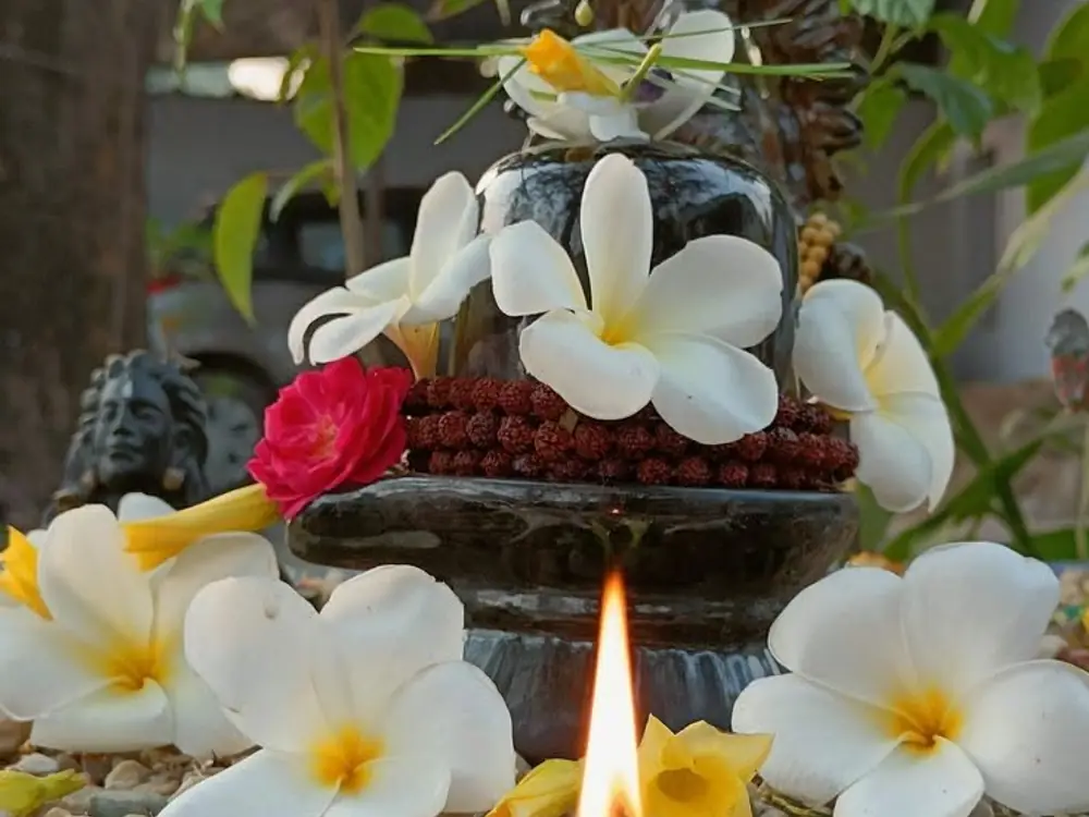 Shivling with white frangipani flowers, rudraksha beads and a lit diya