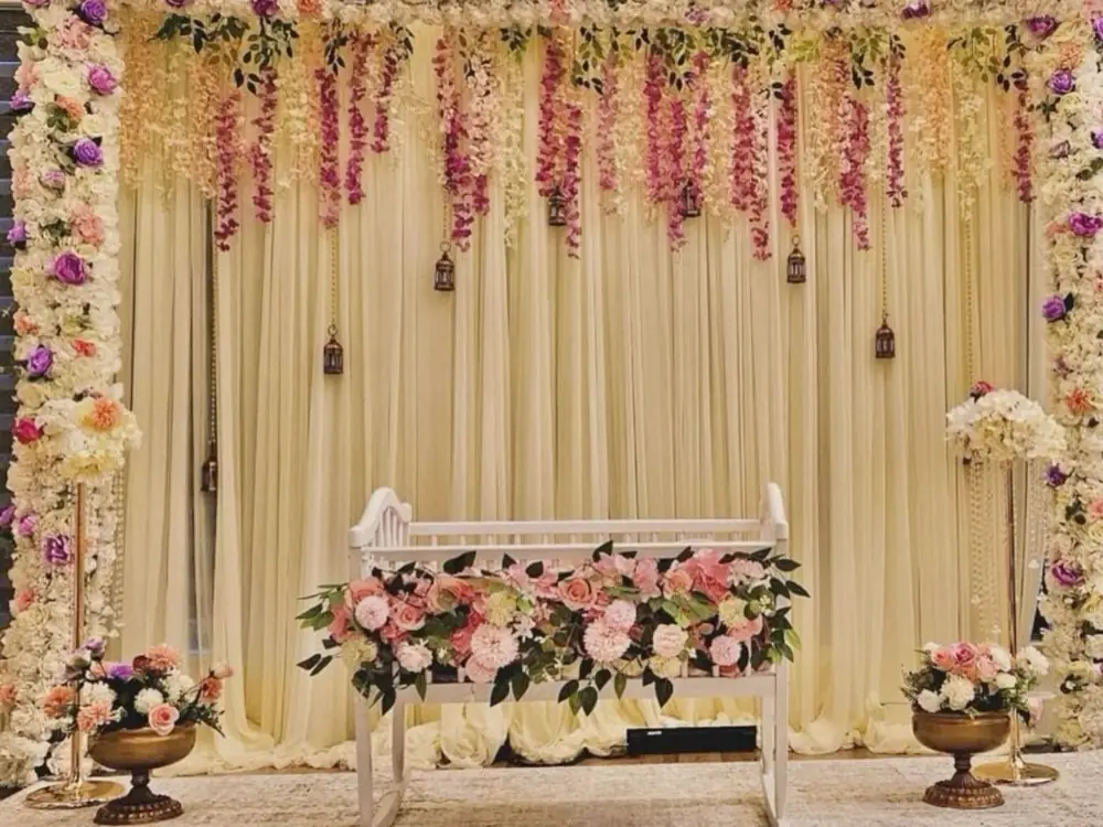 Namkaran setup with an ivory drape, hanging flowers and a cradle of pink roses