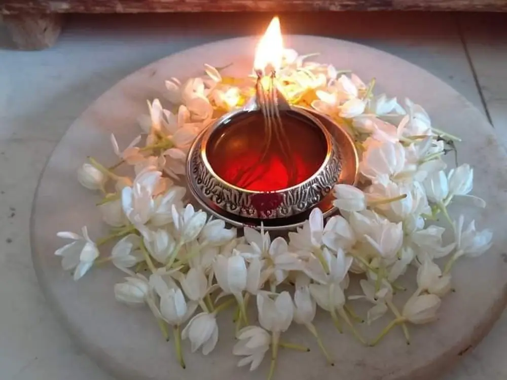 Lit brass diya surrounded by white jasmine flowers on a marble slab